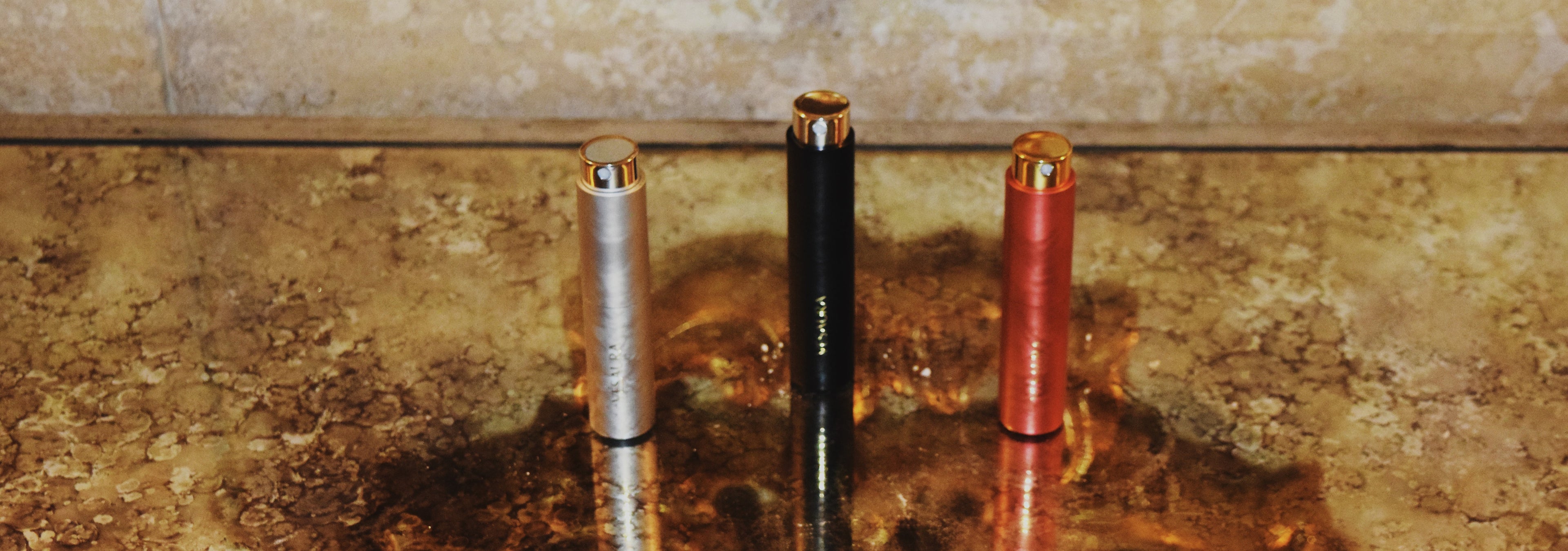 Three Vésaura perfume cases in silver, black, and red displayed against a gold luxury background, showcasing a bold and elegant trio of fragrances.