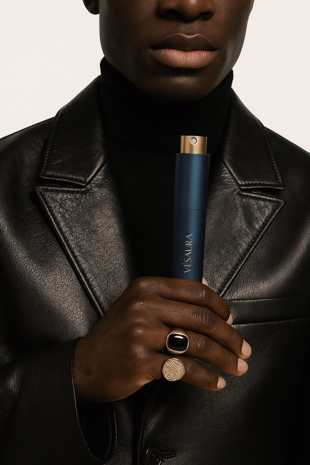 Black model dressed in all black with a leather jacket and gold rings, holding the Vésaura Midnight perfume case, exuding a sleek and edgy vibe.