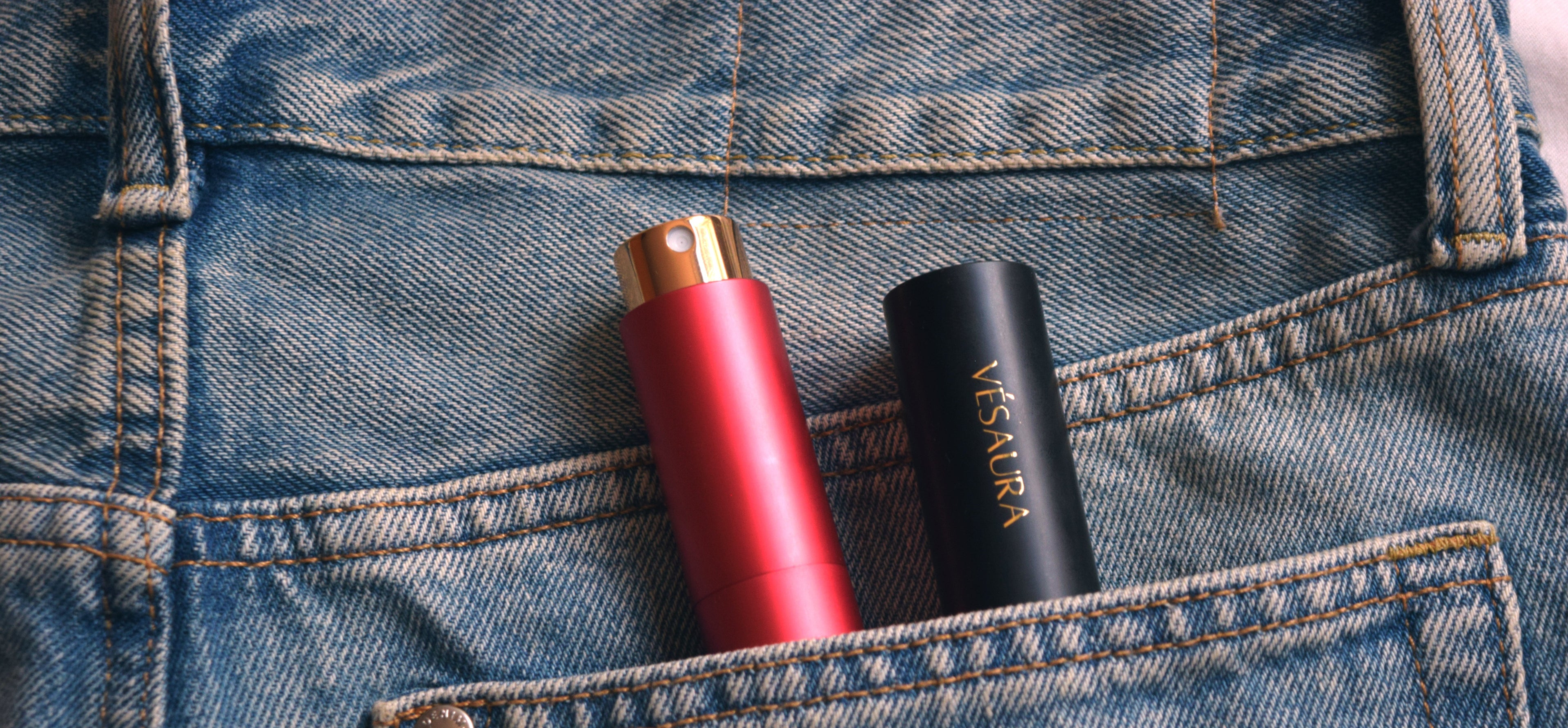 Vésaura perfume cases in Ruby red and Onyx black tucked into the back pocket of a pair of jeans, showcasing sleek and stylish portability.